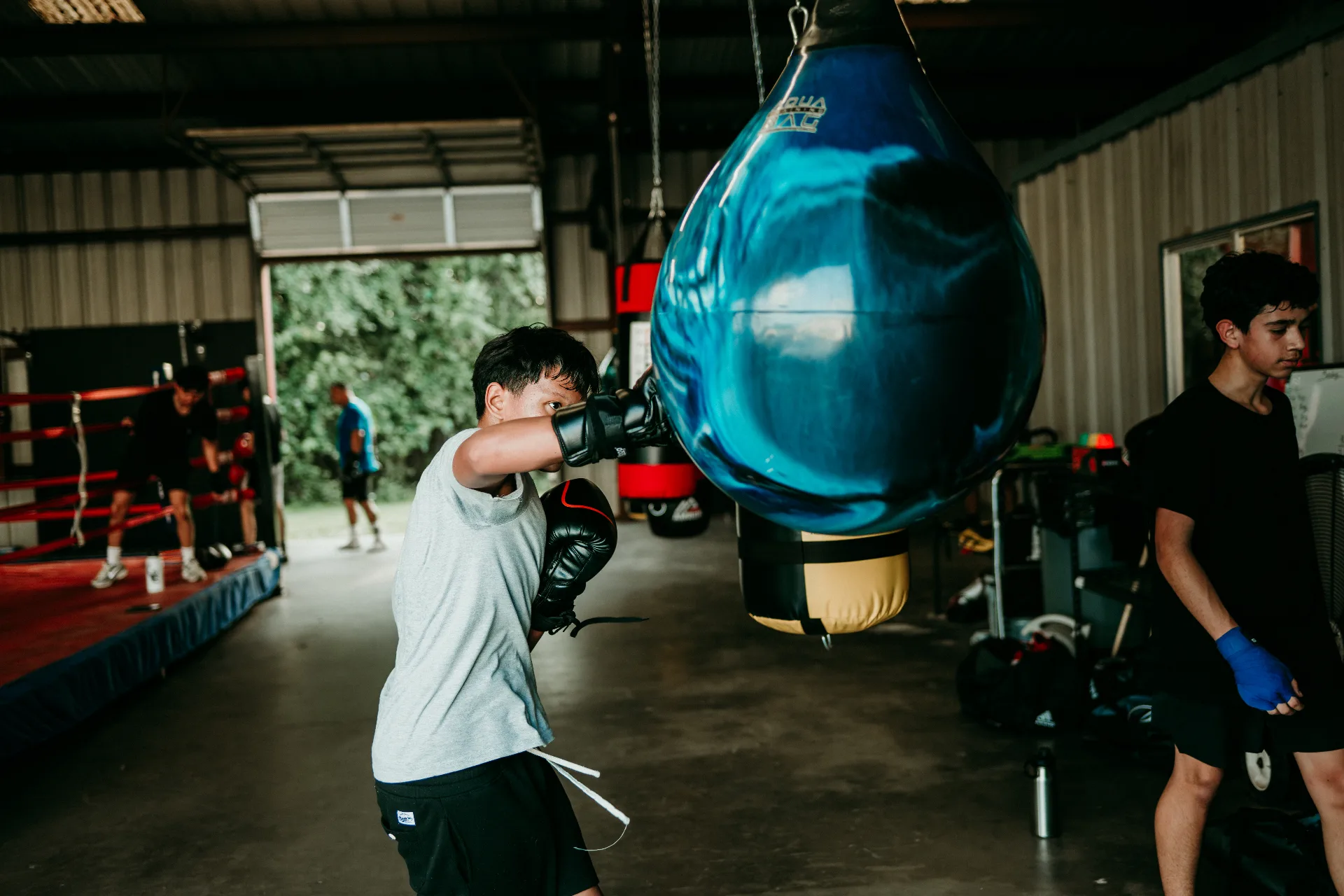 Young boxer working the aqua bag while other athletes train in the background
