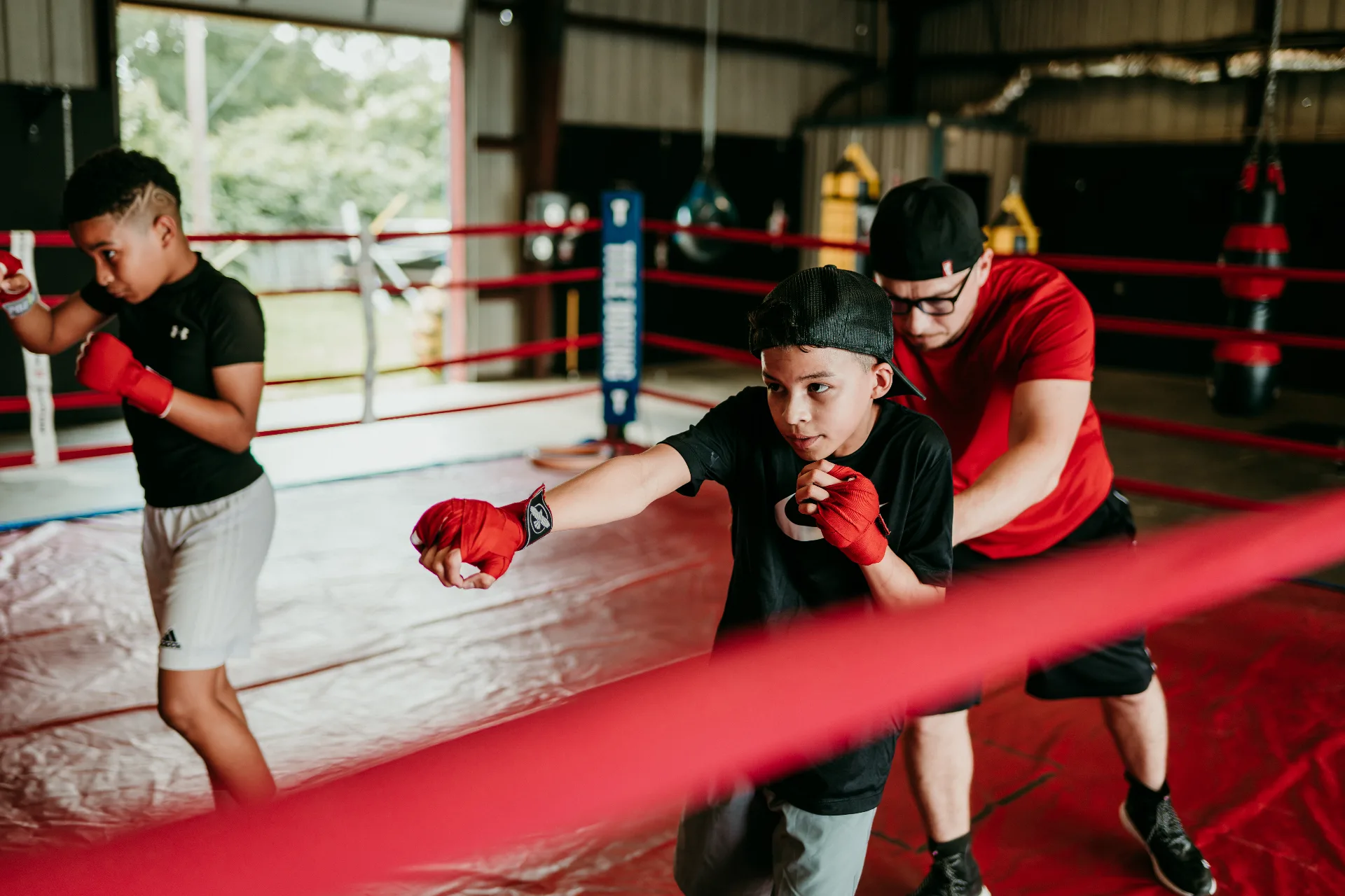 Coach Romo guiding two young boxers through punch technique inside the ring