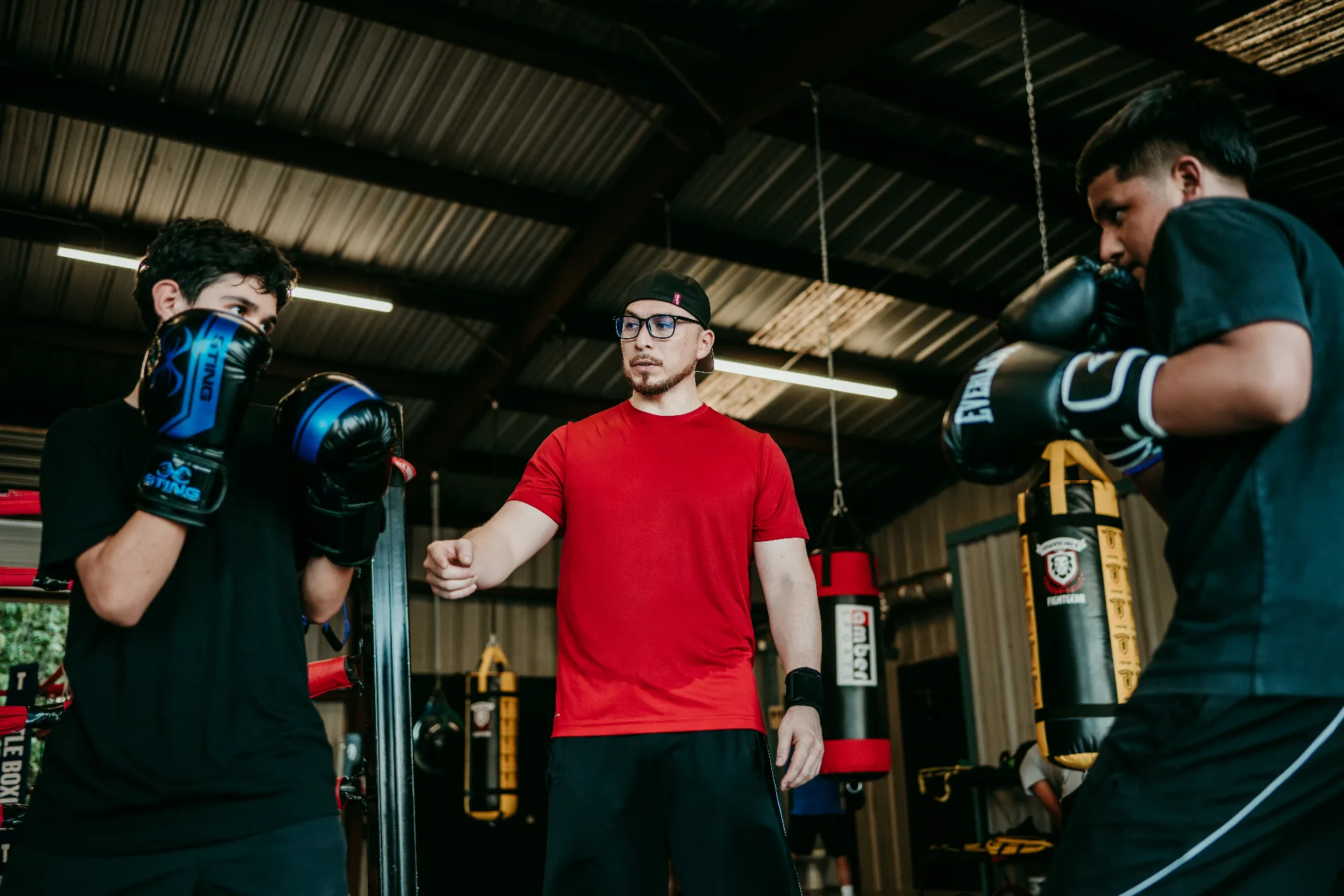 Coach Rodrigo Romo coaching two young boxers during a sparring drill at One More Round Boxing Gym in Tomball, Texas